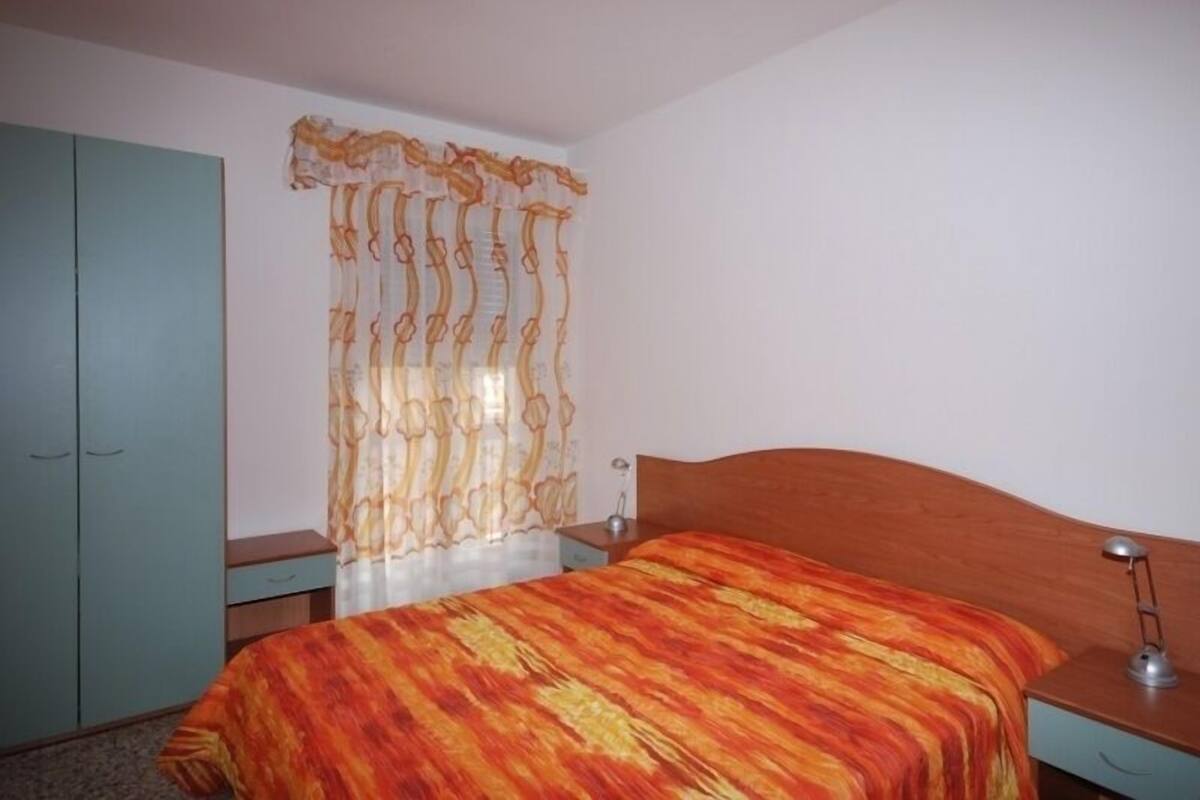 Ein Schlafzimmer mit Bett, Nachttisch, Kleiderschrank und Vorhang.