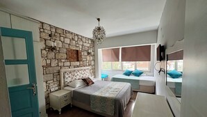 A bedroom with a stone wall, a bed with a floral headboard, a bedside table, a dresser, and a window with a view. - Alacati Sardunya Hotel (Cesme)
