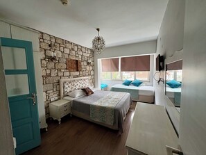 A bedroom with a stone wall, a bed with a floral headboard, a bedside table, a dresser, and a window with a view.