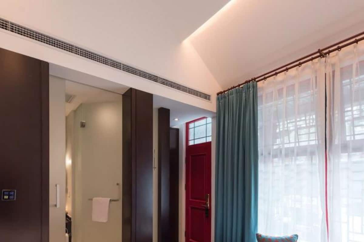 A hotel room with a bed, a sofa, a red door, and a window with curtains.