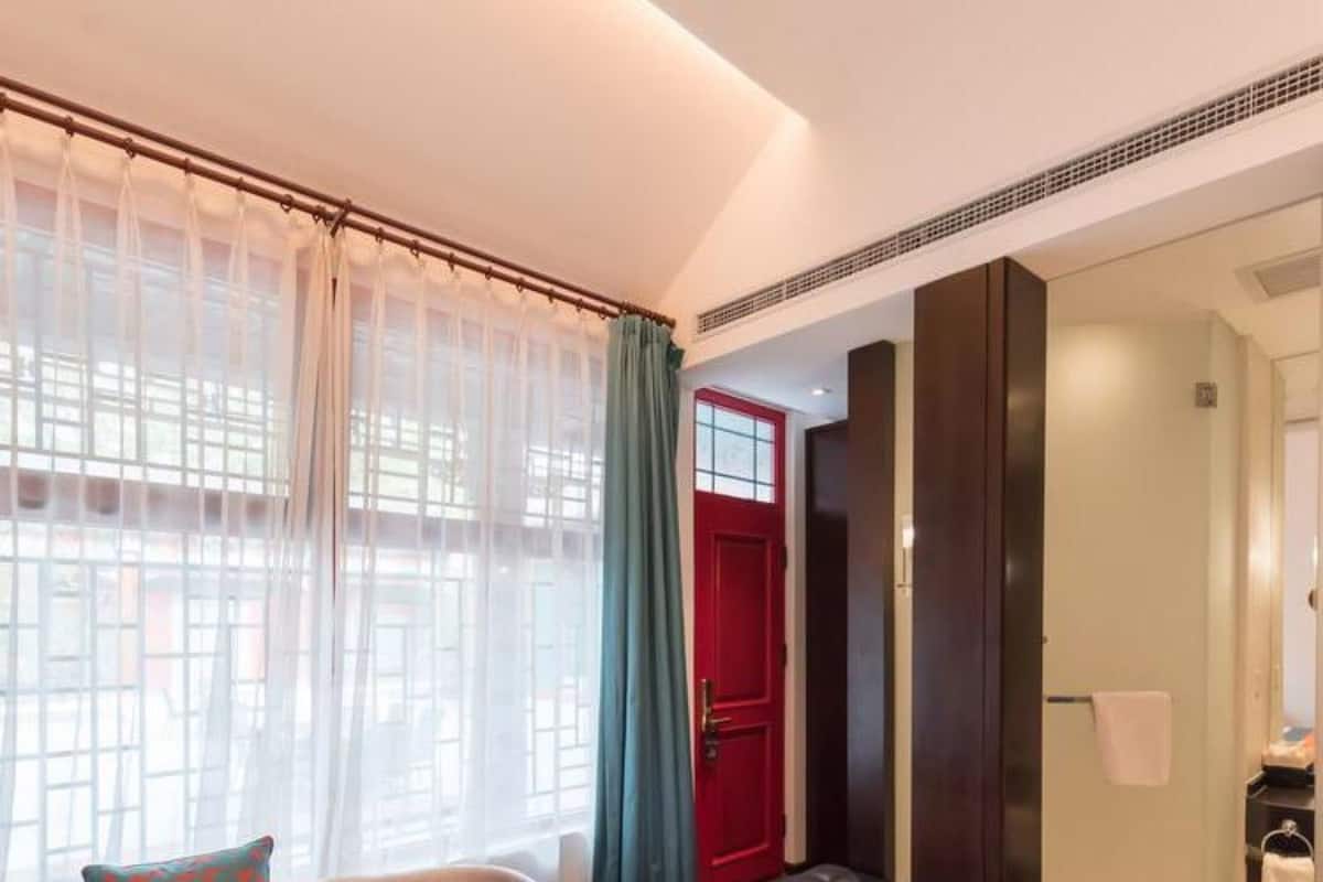 A bedroom with a bed, a sofa, a red door, and a window with sheer curtains.