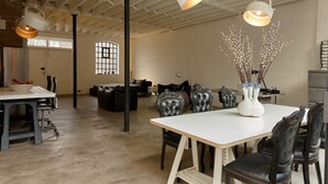 A spacious room with a high ceiling, a white table, black leather chairs, and a vase with branches.