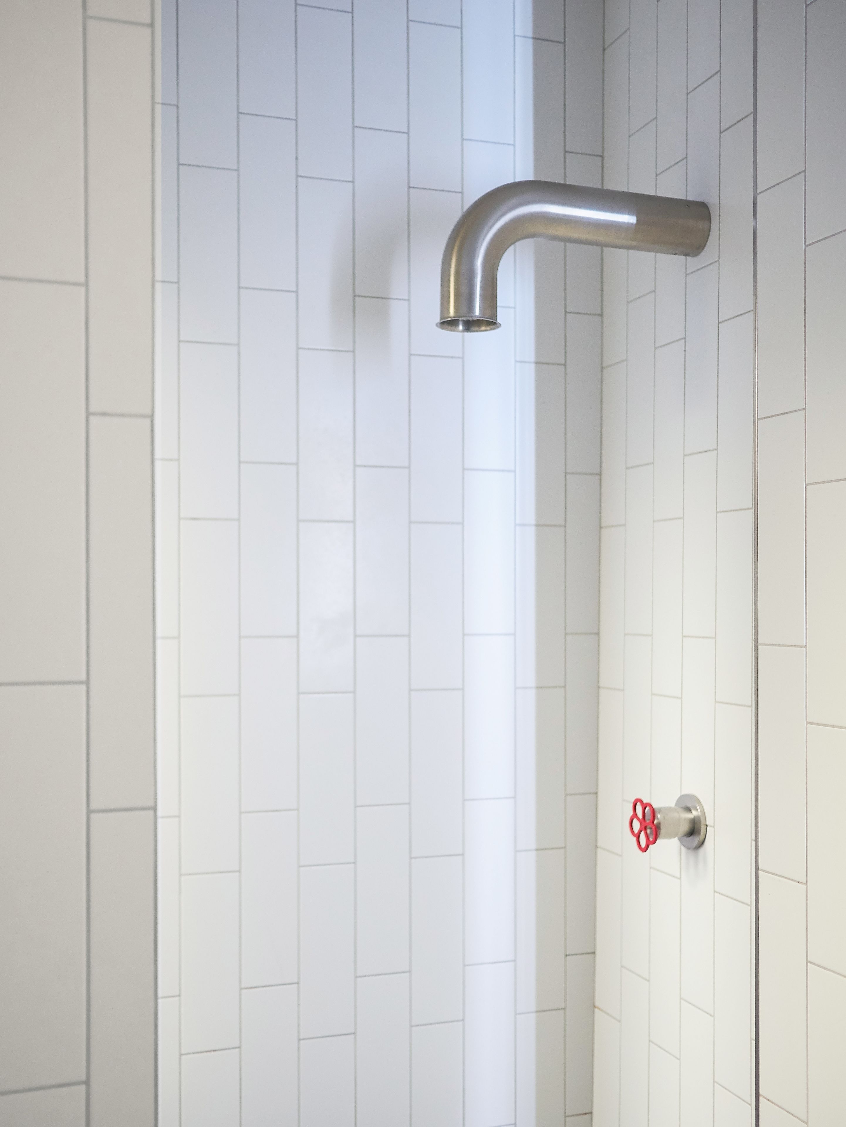 Ein modernes Badezimmer mit weißen Fliesenwänden und einem Duschkopf in gebogener Form.