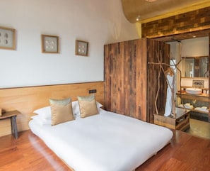 Un cuarto de hotel con una cama grande, cabecera de madera, un armario de madera, una tocador de madera con espejo y cuadros enmarcados en la pared.
