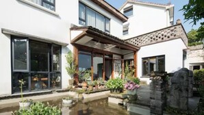A white building with large windows and a covered porch with potted plants. - Floral Hotel Yuequ Yunshang (Hangzhou)