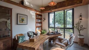 A cozy room with a wooden desk, leather chairs, a bookshelf, and large windows offering a view of greenery. - Floral Hotel Yuequ Yunshang (Hangzhou)