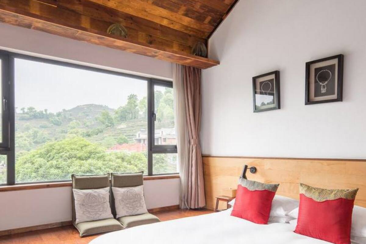 Un dormitorio con un ventanal grande, techo de madera y una cama con almohadas rojas y blancas.