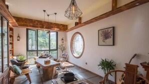 A spacious living area with a wooden dining table, comfortable seating, large windows, and a view of greenery. - Floral Hotel Yuequ Yunshang (Hangzhou)