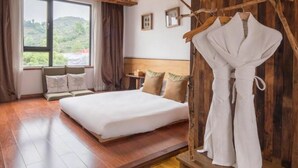 A bedroom with a large bed, wooden flooring, a view of greenery outside, and a wooden wall with a branch decoration. - Floral Hotel Yuequ Yunshang (Hangzhou)