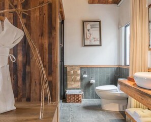 Un baño con techo de madera, inodoro blanco, lavamanos con encimera de madera y un cuadro enmarcado en la pared.