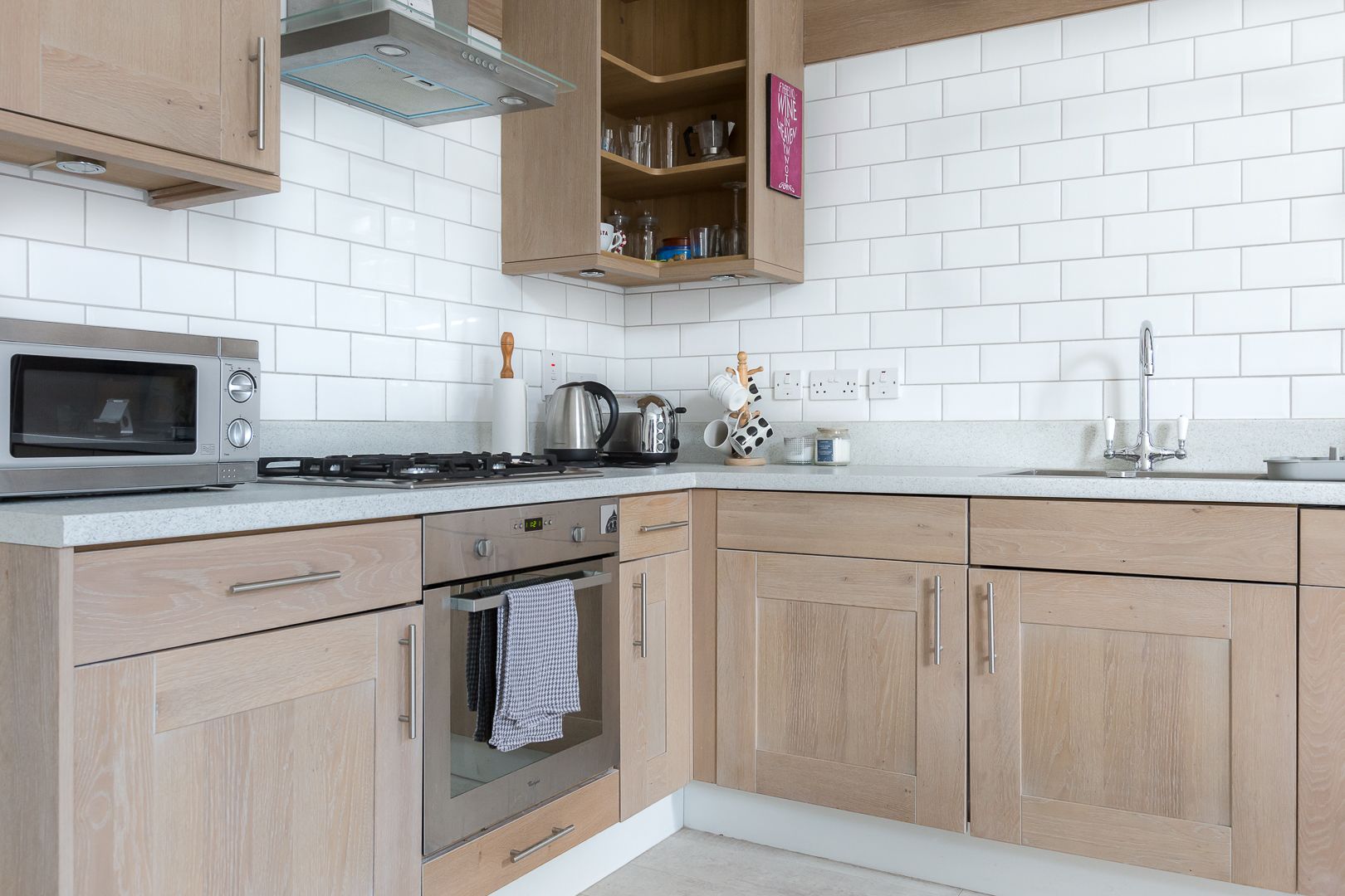 A modern kitchen with wooden cabinets, a stainless steel microwave, a gas stove, and white tiled backsplash.