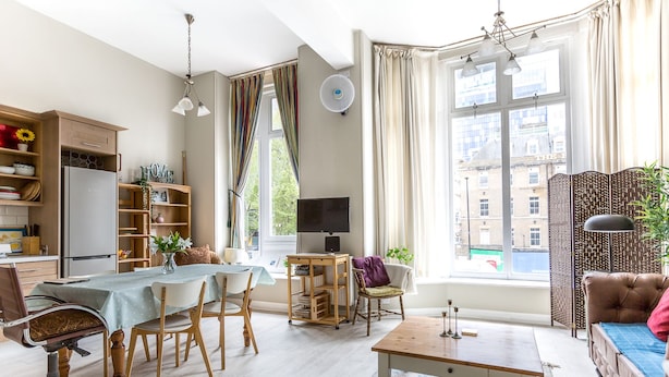 A modern living room with a dining area, a sofa, a TV, and a view of the city through large windows. - Bright Two BR Period Apartment in Whitechapel (London)