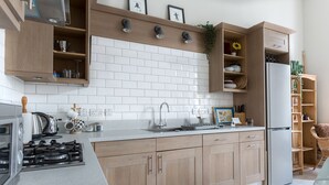 A modern kitchen with wooden cabinets, a stainless steel refrigerator, a gas stove, and a white tiled backsplash. - Bright Two BR Period Apartment in Whitechapel (London)
