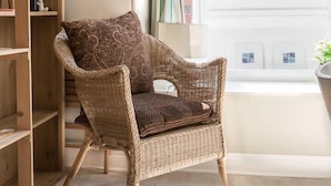 A wicker chair with a patterned cushion in a room with a wooden bookshelf and a window with curtains. - Bright Two BR Period Apartment in Whitechapel (London)