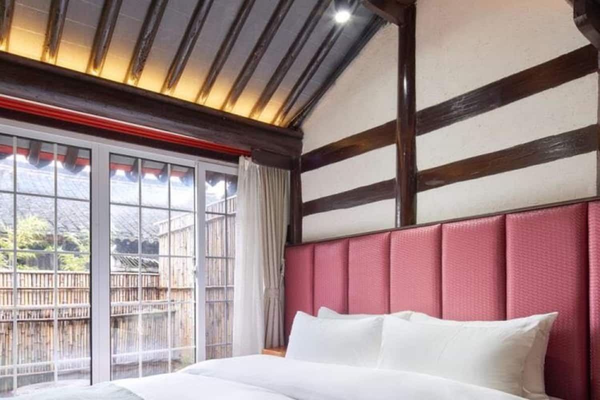 A bedroom with a large bed, a view through a sliding glass door, and a sloped ceiling with exposed beams.