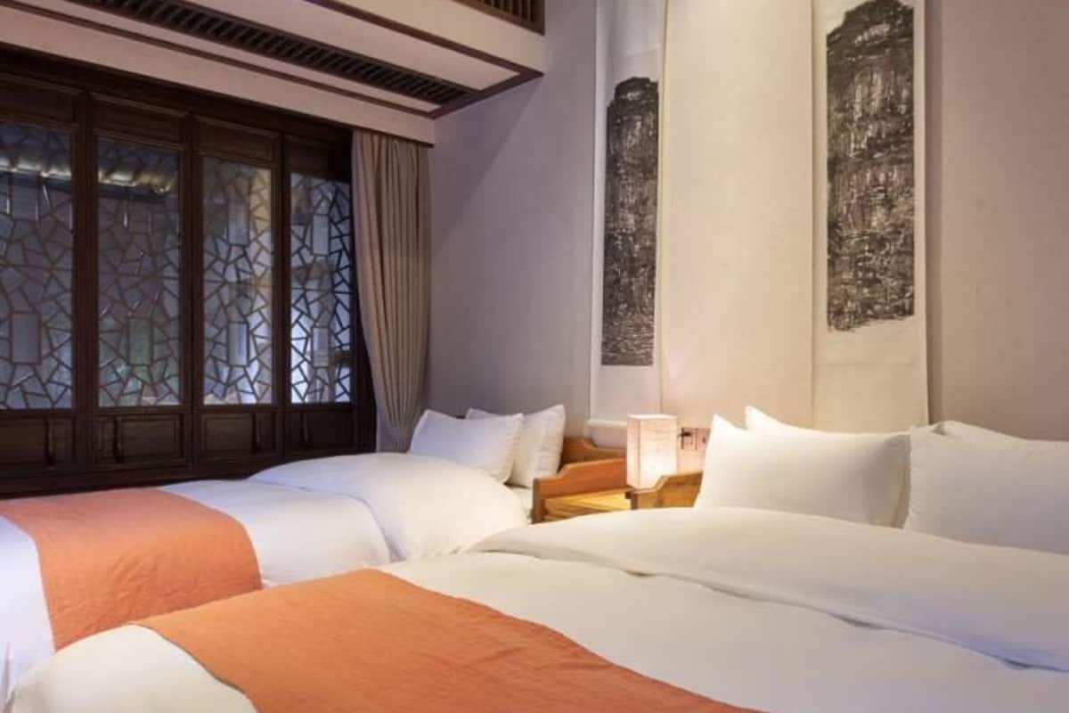 A hotel room with two beds, a nightstand, and a window with decorative glass.