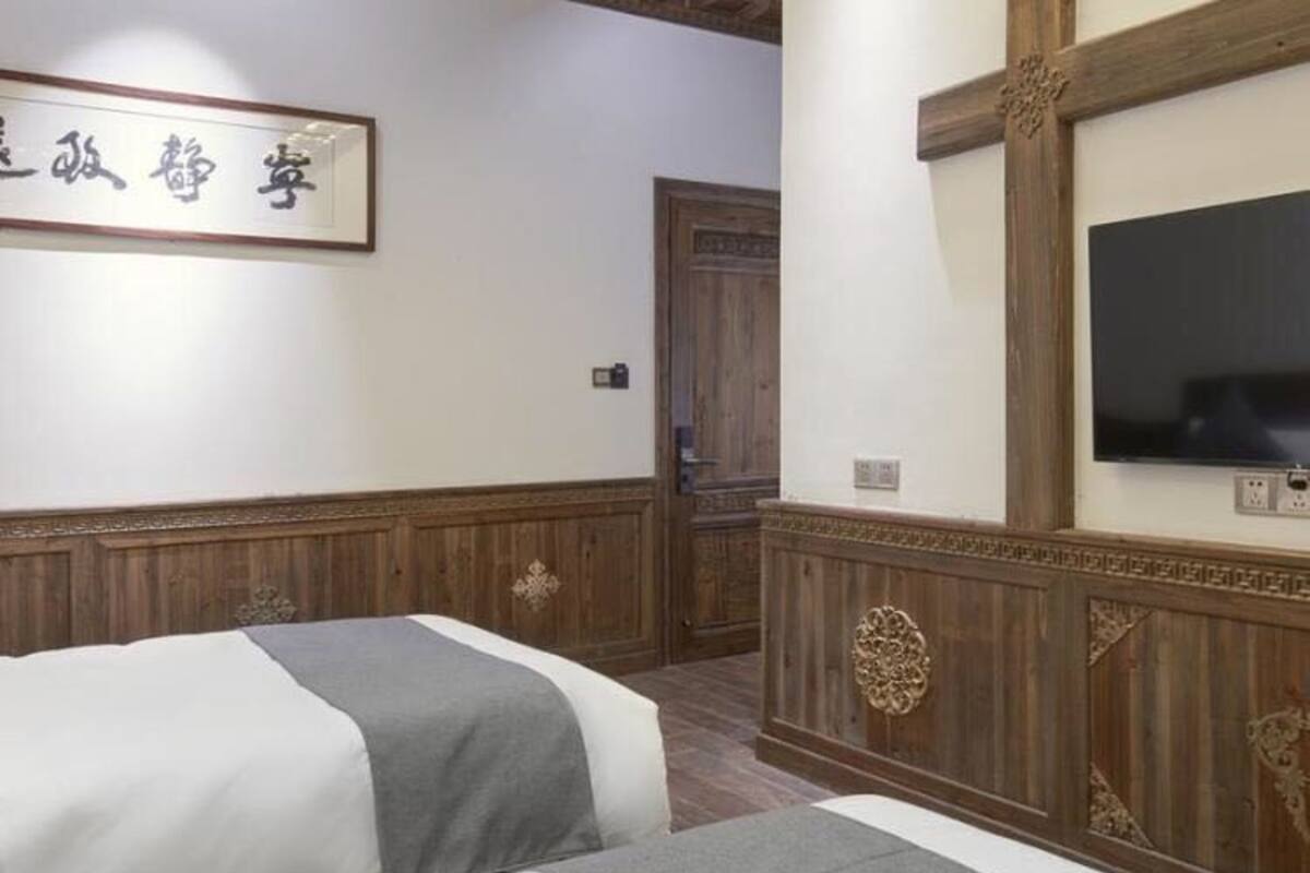 Une chambre d’hôtel avec deux lits, des panneaux de bois, une télévision et une enseigne avec des caractères chinois.