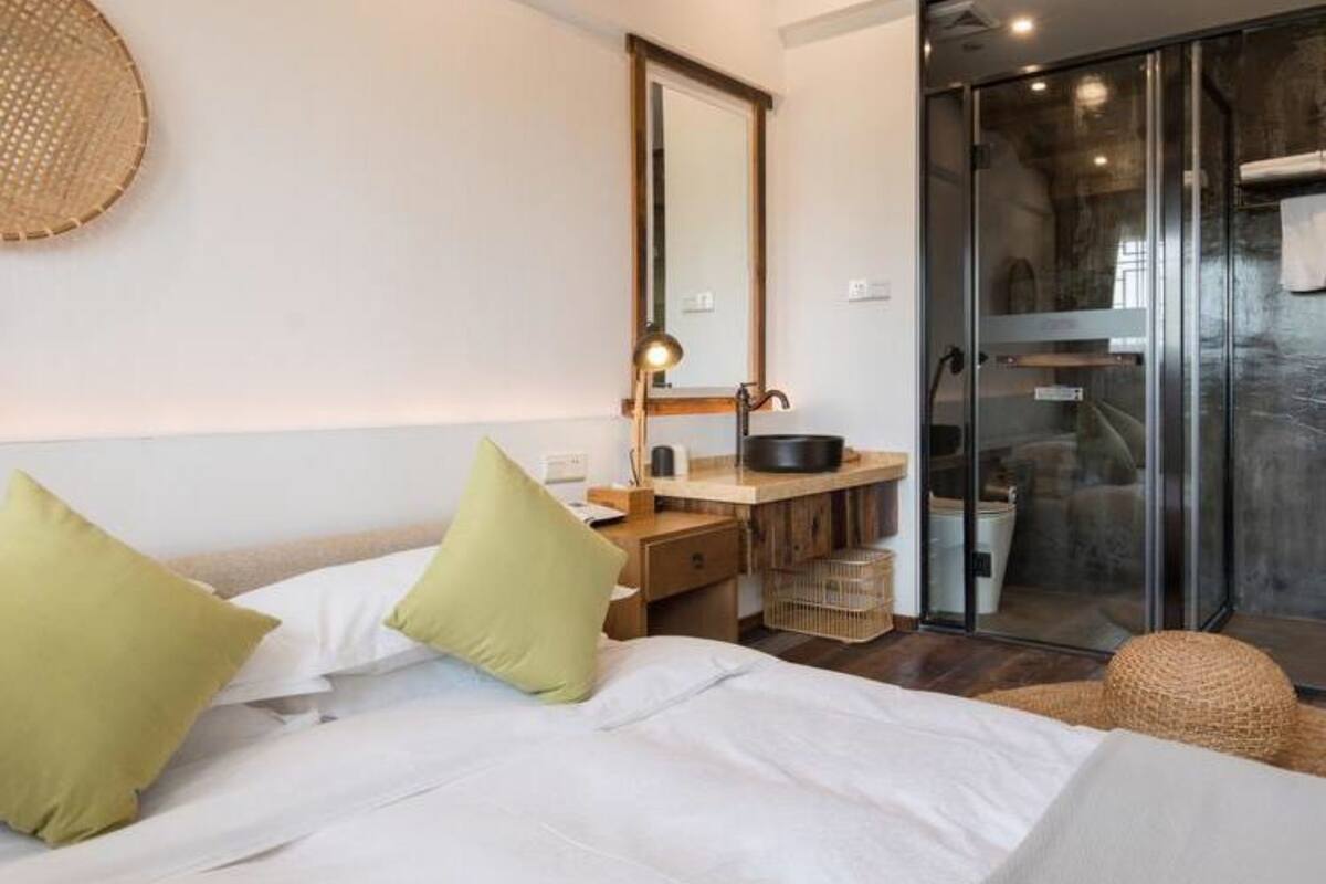 A modern hotel room with a bed, a desk with a mirror, a sink, and a sliding glass door leading to a balcony.