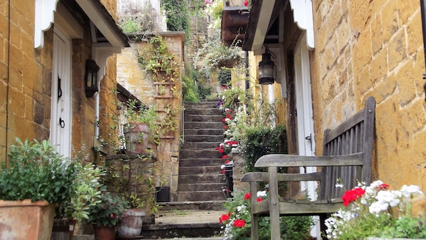 A narrow stone staircase with steps leading up to a wooden door, flanked by potted plants and flowers. - Bridge Farm Holiday Cottages (Evesham)