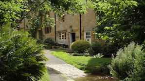 A stone building with a traditional design, a paved pathway leading to the entrance, and lush greenery surrounding the property. - Bridge Farm Holiday Cottages (Evesham)