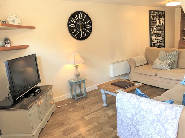 A living room with a flat-screen TV, a lamp, a sofa, a patterned throw, and a wall clock. - Bridge Farm Holiday Cottages (Evesham)