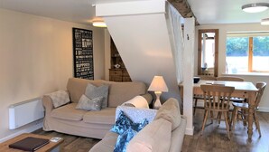 A cozy living room with a sofa, a coffee table, and a dining area with a table and chairs. - Bridge Farm Holiday Cottages (Evesham)
