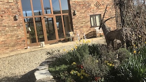 A brick building with large windows, outdoor seating, and a garden with flowers. - Bridge Farm Holiday Cottages (Evesham)