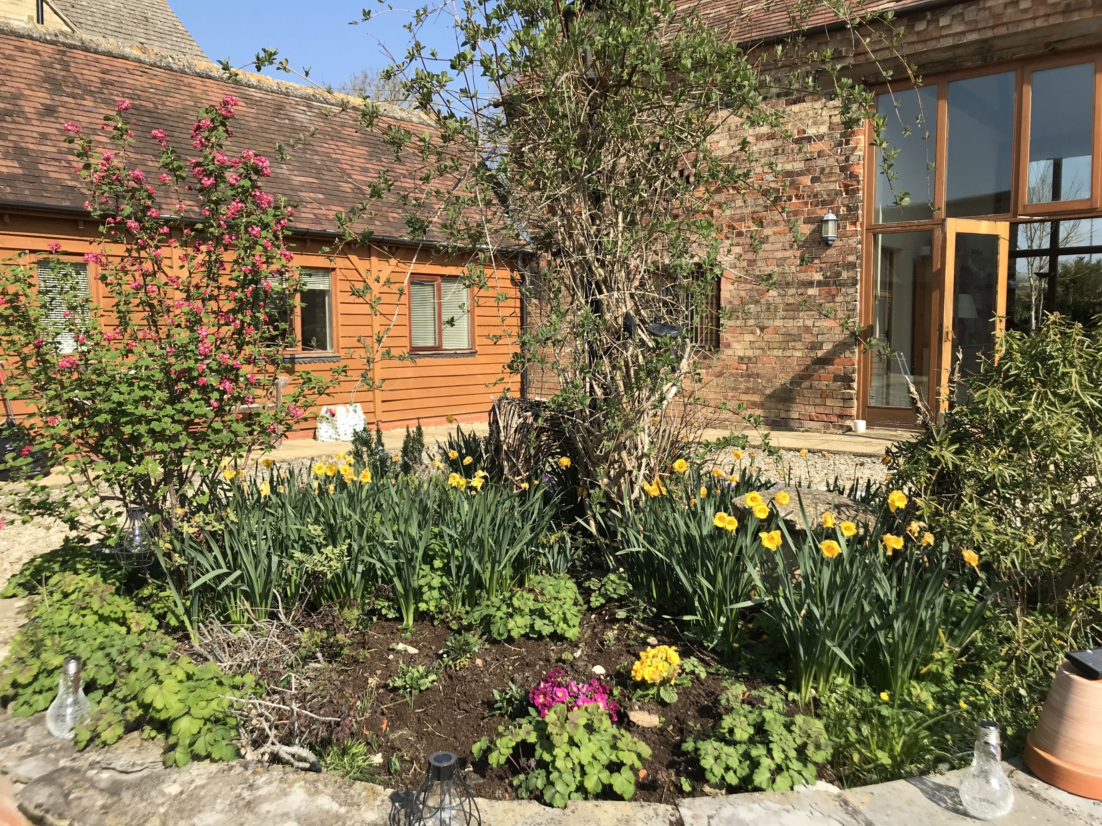 A brick building with a garden in front, featuring various plants and flowers.