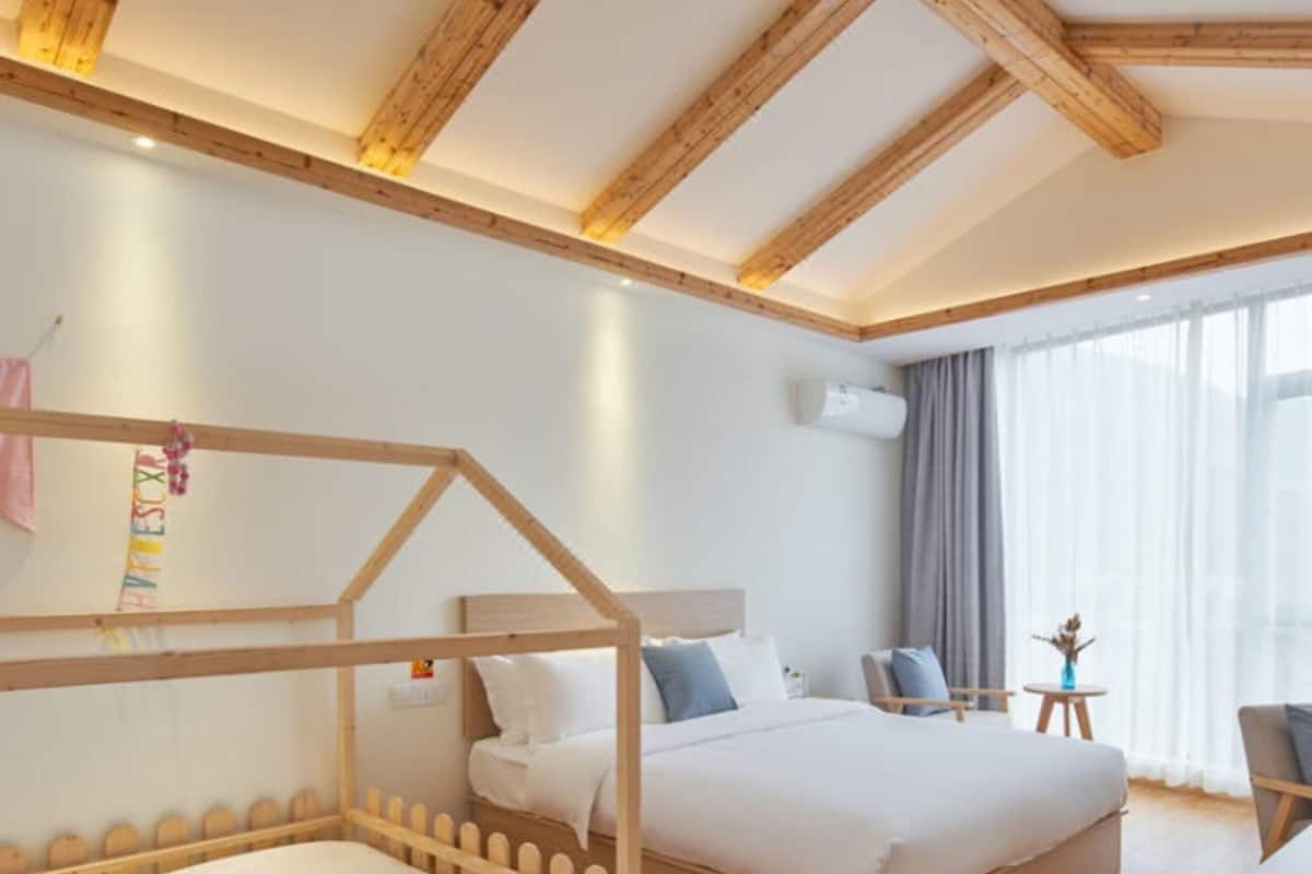 Quarto de hotel com duas camas, vigas de madeira no teto, uma mesinha com um vaso e uma janela com cortinas.