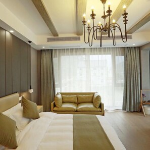 A modern hotel room with a large bed, a sofa, and a chandelier.