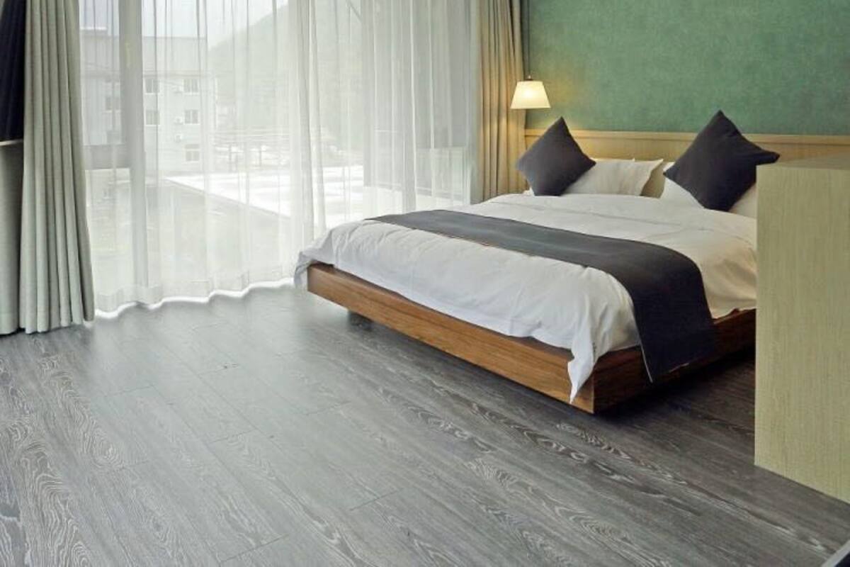 Habitación de hotel moderna con una cama grande, un muro decorativo verde y vistas a través de cortinas translúcidas.