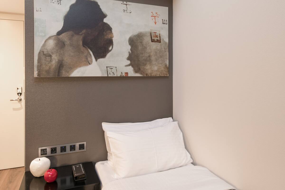 A bedroom with a bed, a nightstand, a wall-mounted painting, and a door.
