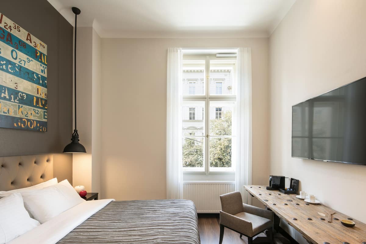 A hotel room with a bed, a desk, a chair, a television, and a window with a view of buildings.