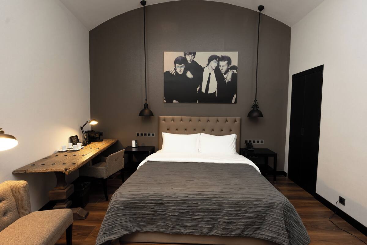 A bedroom with a large bed, a wooden desk, a chair, and a wall-mounted picture.
