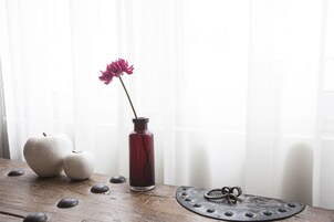 Uma mesa de madeira com duas maçãs, um vaso com uma flor e um prato decorativo com um anel.