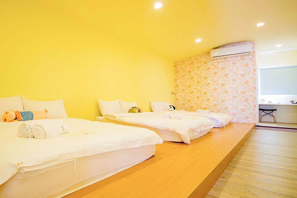 A hotel room with two beds, a wooden floor, a small desk, and an air conditioning unit.