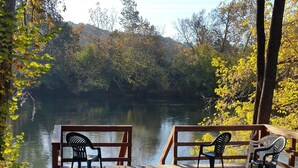 A wooden deck with chairs overlooking a calm lake, surrounded by trees and autumn foliage.