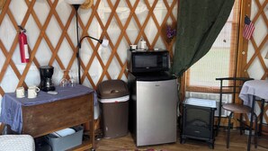 A cozy interior with a wooden lattice wall, a small refrigerator, a microwave, a table with a lamp, and a colorful rug.