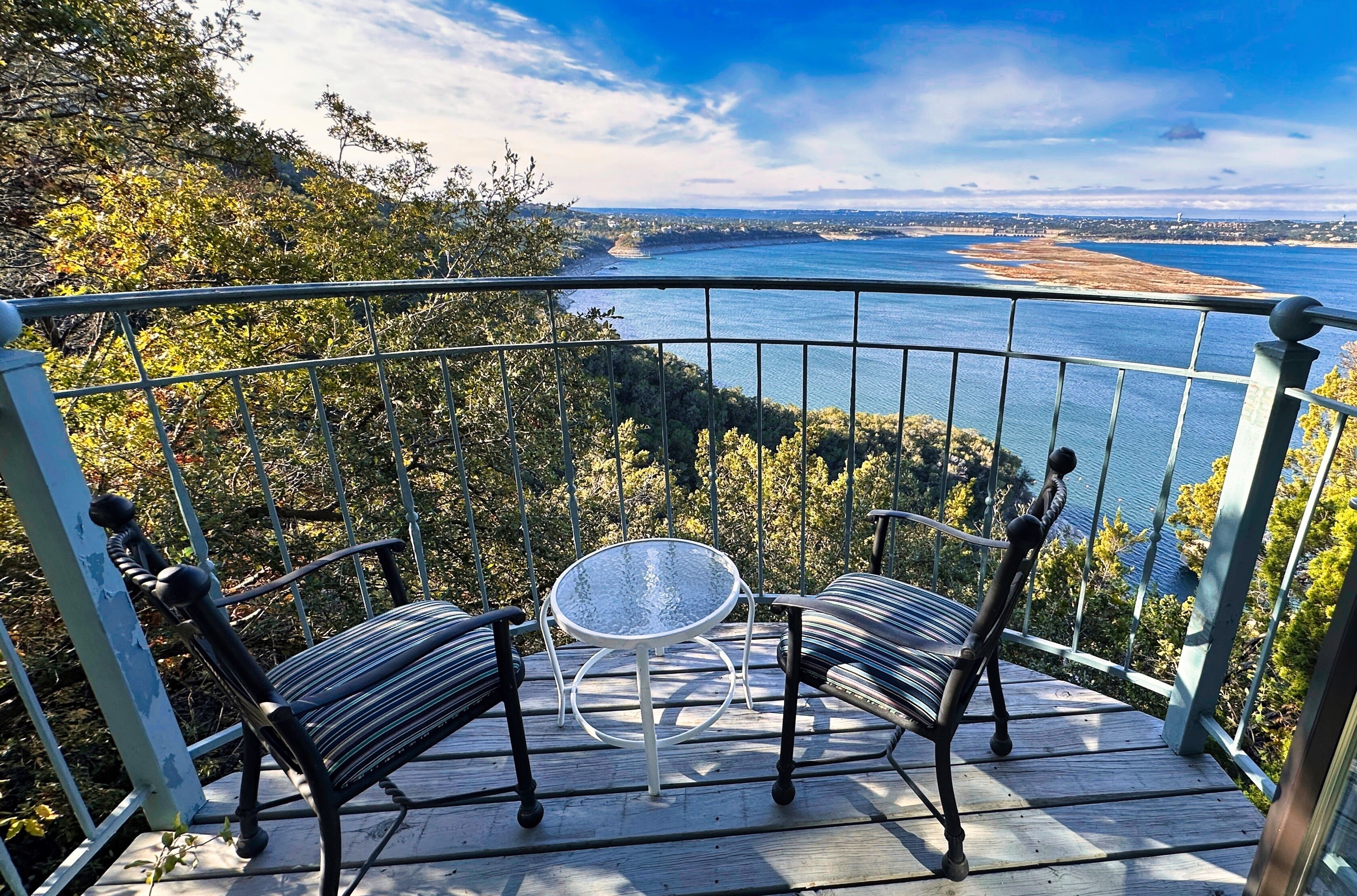 Un balcon donnant sur une étendue d’eau et sur un paysage lointain, aménagé avec deux chaises et une petite table.