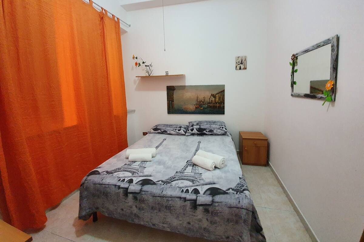 A bedroom with a bed, a nightstand, a mirror, and a painting on the wall.