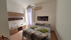 A bedroom with a bed, a nightstand, a lamp, a radio, a picture on the wall, and a window with curtains. - Al Baglio di Maqueda (Palermo)
