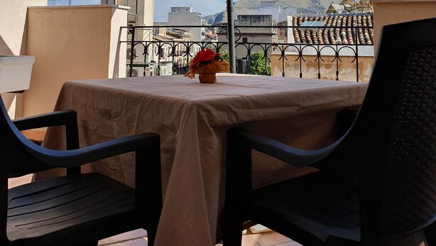 A table with a tablecloth and two chairs under a large umbrella on a balcony with a city view. - Al Baglio di Maqueda (Palermo)