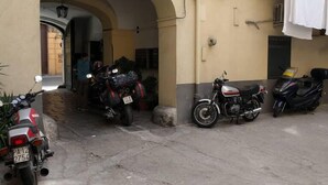 A courtyard with parked motorcycles and a car, an archway entrance, and a building with a balcony. - Al Baglio di Maqueda (Palermo)