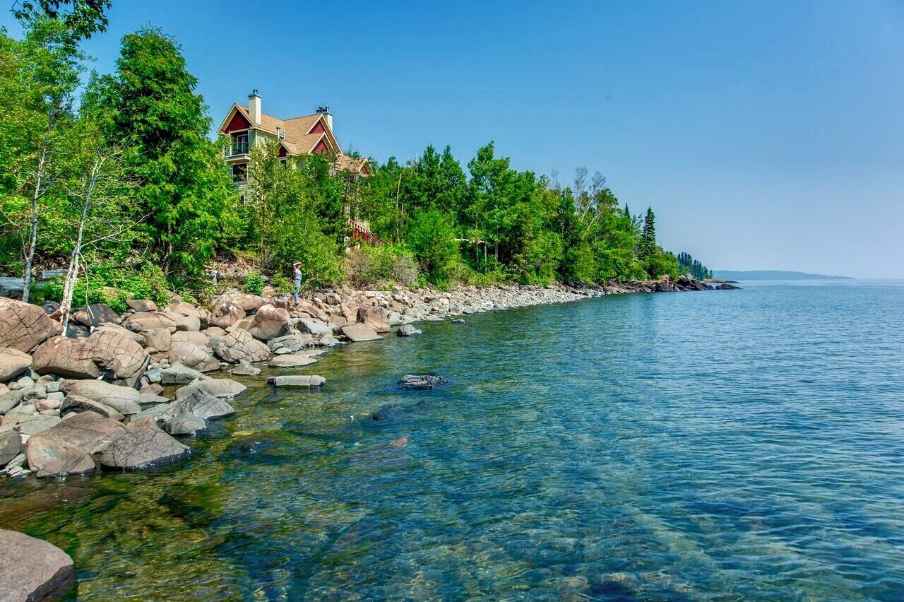 A lakeside property with a house, clear water, and surrounding trees.
