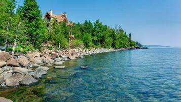A lakeside property with a house, clear water, and surrounding trees.