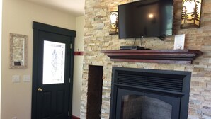 A room with a fireplace, a television mounted on the wall, a door with a window, and a red carpet.
