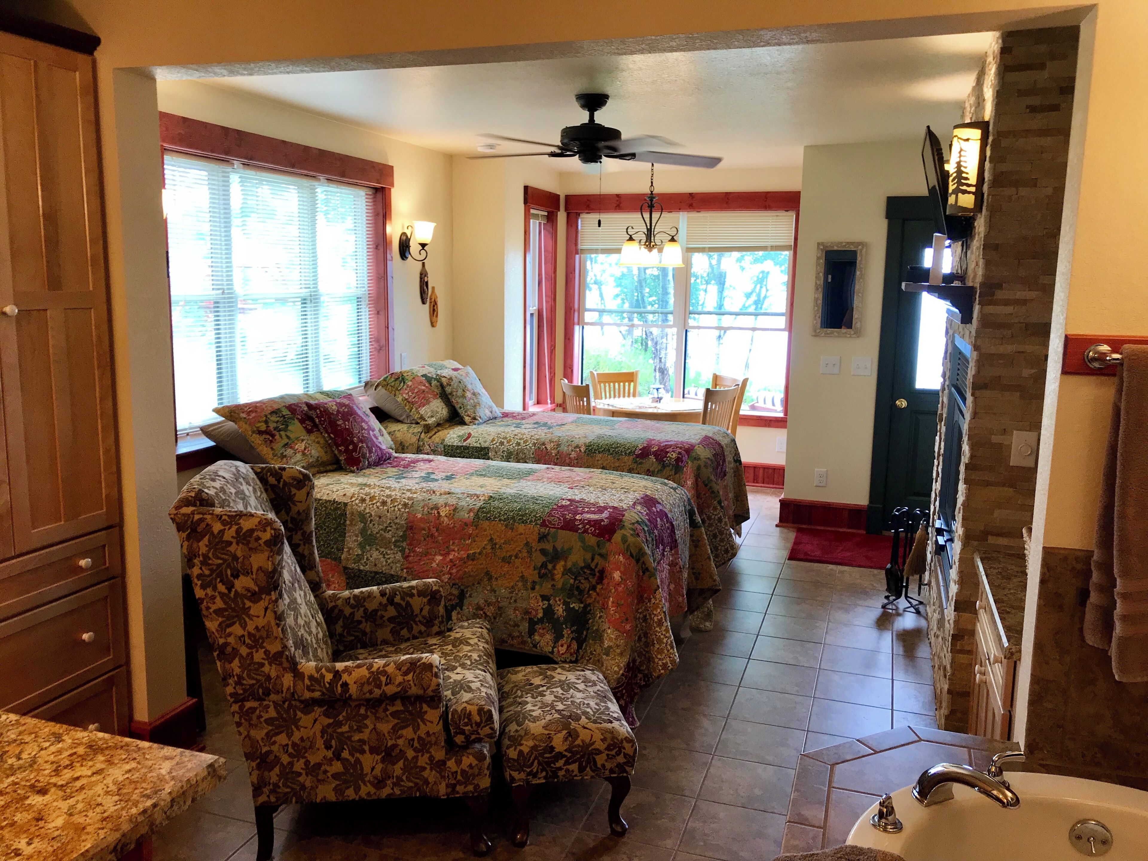 A room with two floral-patterned sofas, a dining table with chairs, a ceiling fan, a fireplace, and a view of the outdoors.