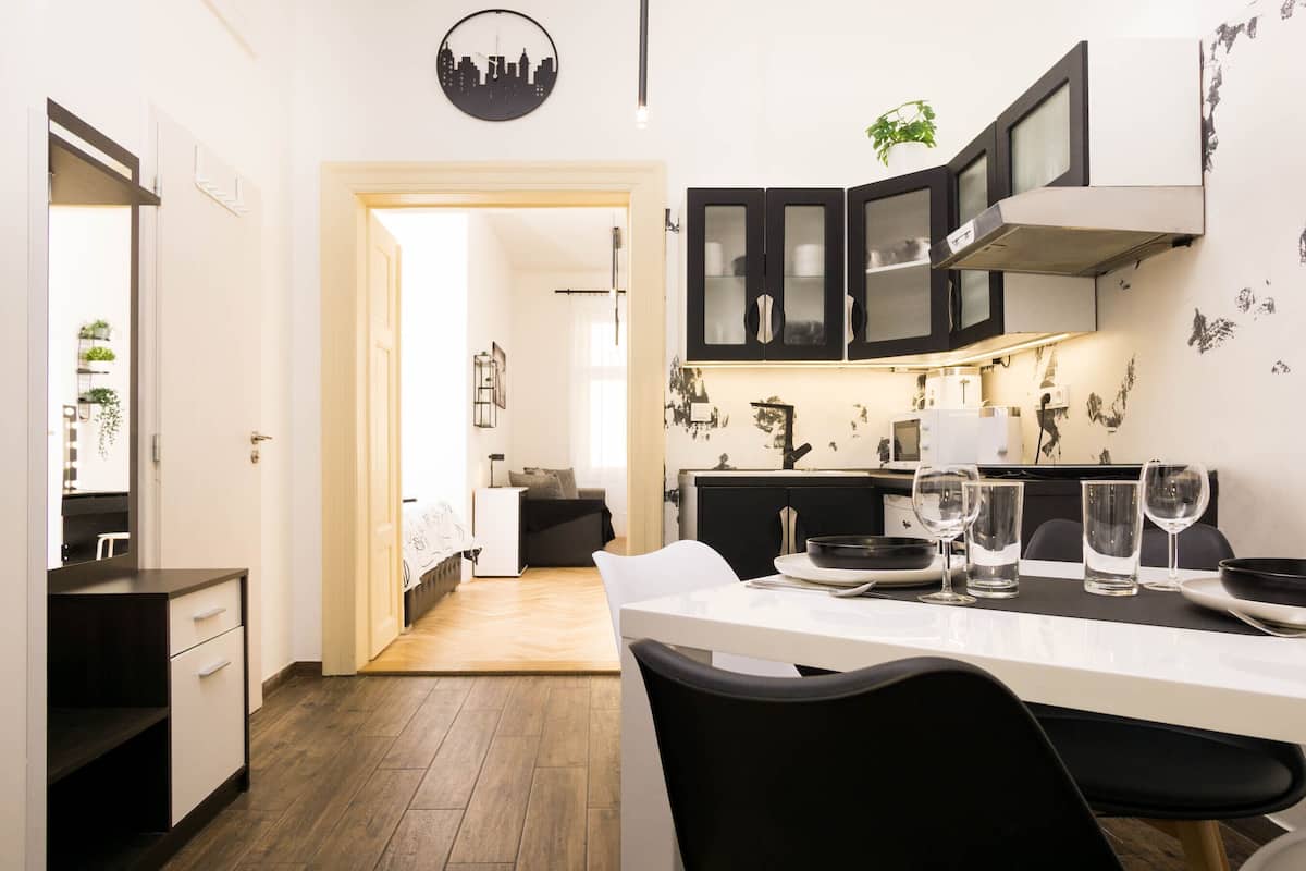 Une cuisine moderne avec une table à manger pour quatre personnes, un meuble noir aux portes en verre et un mur orné d’œuvres d’art abstraites en noir et blanc.