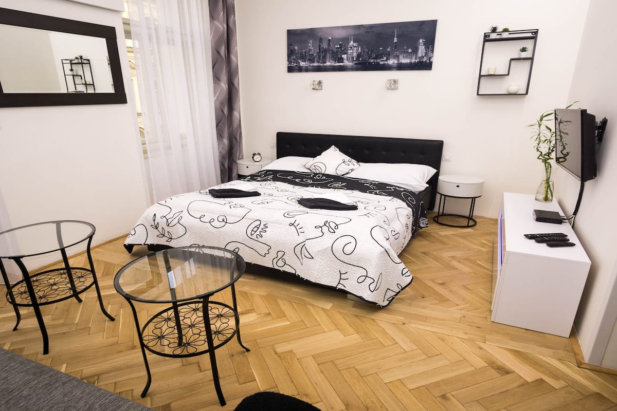 Une chambre à coucher bien rangée, avec un lit, deux tables de chevet, une petite armoire blanche et un téléviseur posé sur un meuble.