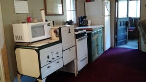 A compact kitchen with a microwave, stove, and refrigerator. There is a calendar on the wall and a window with blinds.